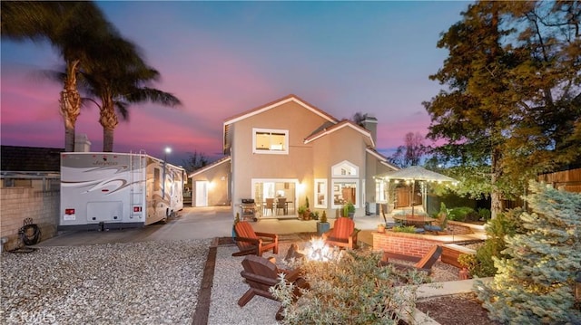 back of property at dusk with a patio, fence, a chimney, stucco siding, and a fire pit