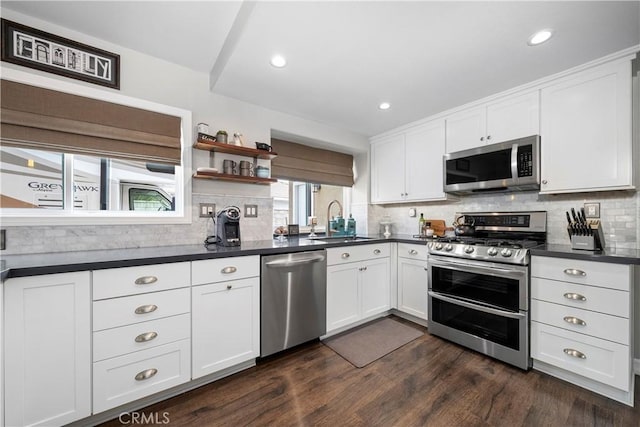 kitchen with white cabinetry, dark countertops, appliances with stainless steel finishes, and a sink