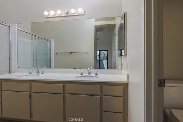 full bathroom with double vanity, an enclosed shower, toilet, and a sink