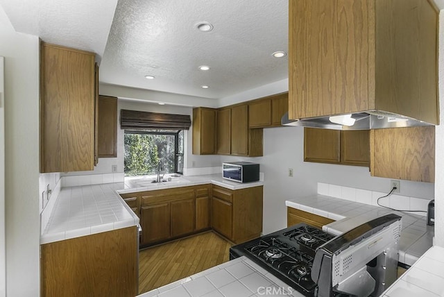 kitchen featuring a sink, tile counters, brown cabinetry, and custom range hood