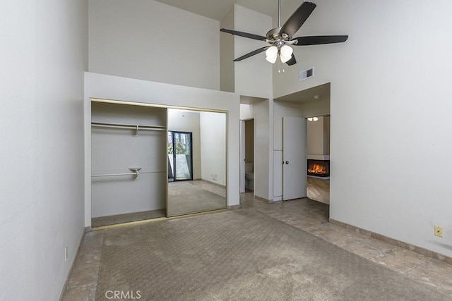 unfurnished bedroom with visible vents, a closet, carpet floors, a lit fireplace, and a towering ceiling