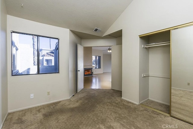 unfurnished bedroom featuring carpet, visible vents, lofted ceiling, a warm lit fireplace, and a closet