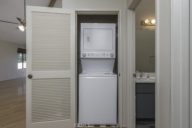 clothes washing area with stacked washer and clothes dryer, a ceiling fan, a sink, wood finished floors, and laundry area