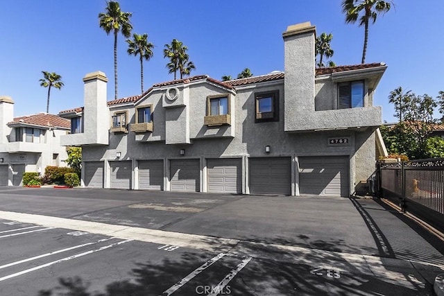 back of house featuring fence, a residential view, a tile roof, stucco siding, and a chimney