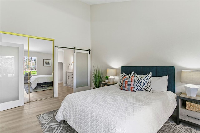 bedroom with wood finished floors, a barn door, a closet, a high ceiling, and baseboards