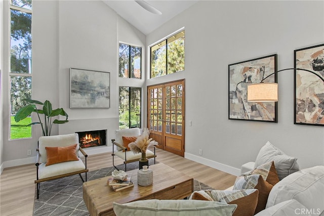 interior space featuring baseboards, a lit fireplace, wood finished floors, and high vaulted ceiling