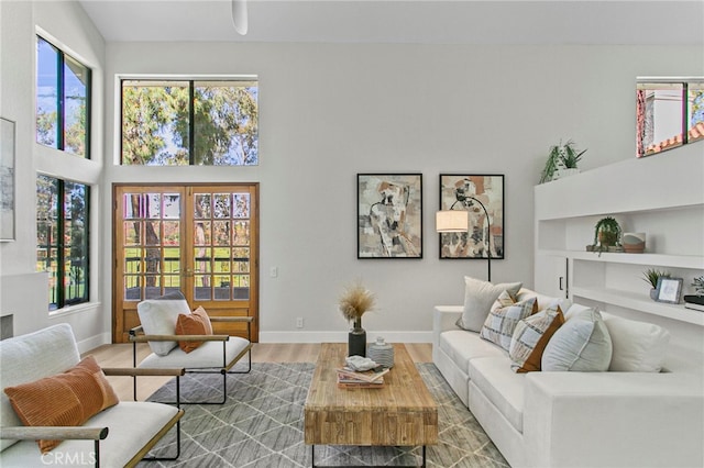 living room featuring french doors, baseboards, a high ceiling, and wood finished floors