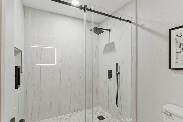 bathroom with a marble finish shower, toilet, and a textured wall