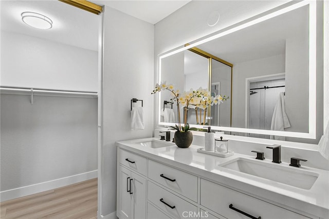 full bathroom featuring double vanity, wood finished floors, baseboards, and a sink