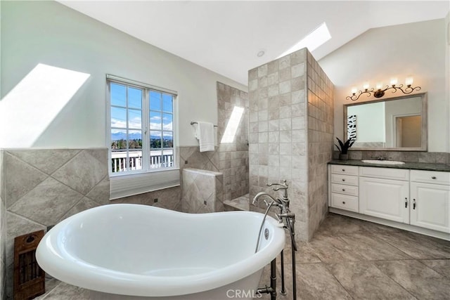 full bathroom featuring vaulted ceiling with skylight, a freestanding bath, tile walls, and vanity