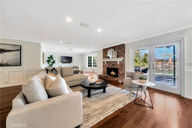 living area featuring recessed lighting, ornamental molding, dark wood-type flooring, a brick fireplace, and a decorative wall