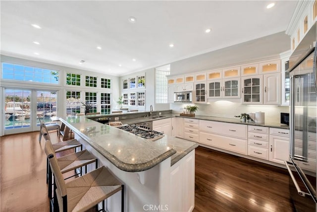 kitchen with dark wood-type flooring, a sink, white cabinetry, appliances with stainless steel finishes, and a peninsula