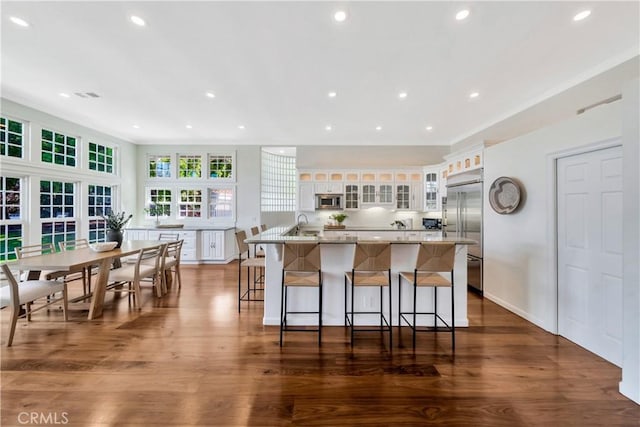 kitchen with built in appliances, white cabinetry, a breakfast bar, and dark wood-type flooring