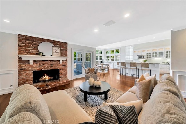 living room featuring a brick fireplace, ornamental molding, wainscoting, wood finished floors, and a decorative wall