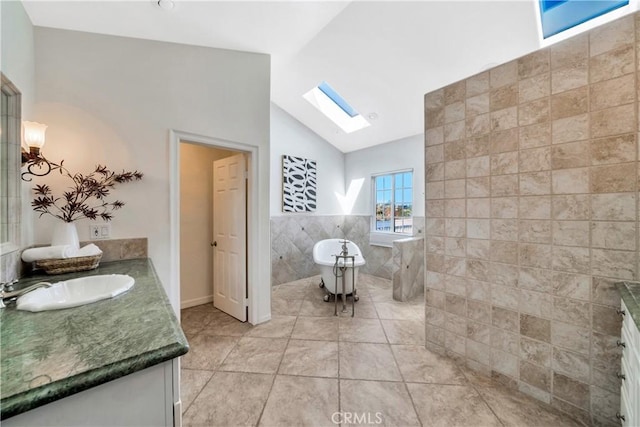 bathroom featuring tile patterned floors, lofted ceiling with skylight, tile walls, a freestanding bath, and vanity