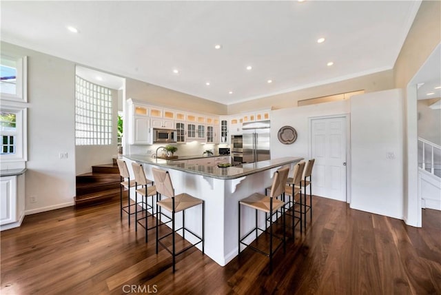 kitchen with a breakfast bar area, dark wood-style floors, built in appliances, and ornamental molding