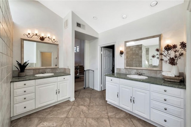 bathroom with vaulted ceiling, two vanities, visible vents, and a sink