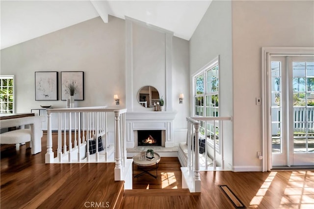 living area featuring beamed ceiling, wood finished floors, a large fireplace, and a healthy amount of sunlight