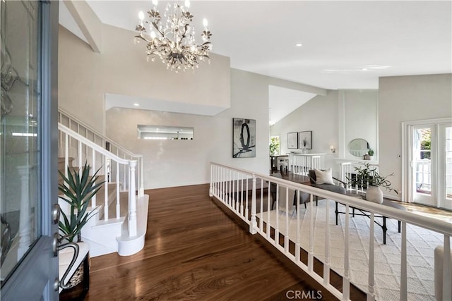 corridor with a chandelier, vaulted ceiling, stairway, and wood finished floors