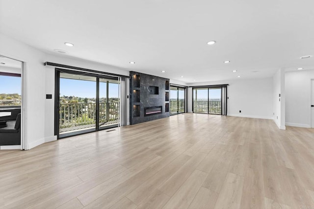 unfurnished living room featuring plenty of natural light, light wood-style floors, recessed lighting, and a large fireplace