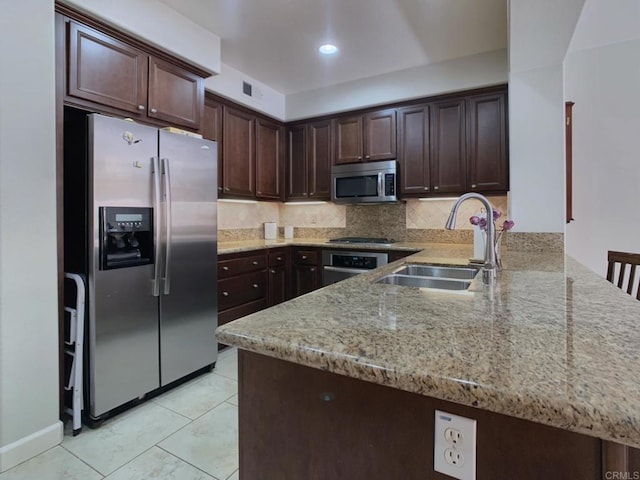 kitchen featuring dark brown cabinets, light stone counters, appliances with stainless steel finishes, a peninsula, and a sink