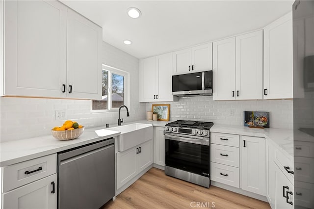 kitchen featuring white cabinets, stainless steel appliances, light wood-style floors, and a sink