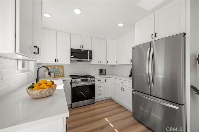 kitchen with tasteful backsplash, stainless steel appliances, light wood-style floors, white cabinetry, and a sink