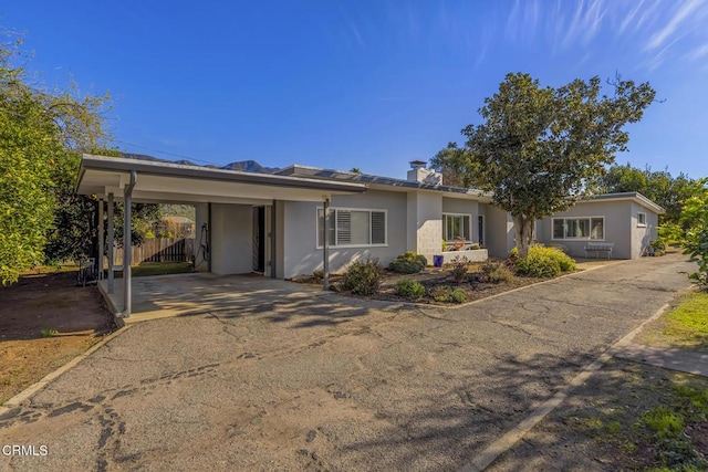 ranch-style home with a carport, fence, driveway, and stucco siding