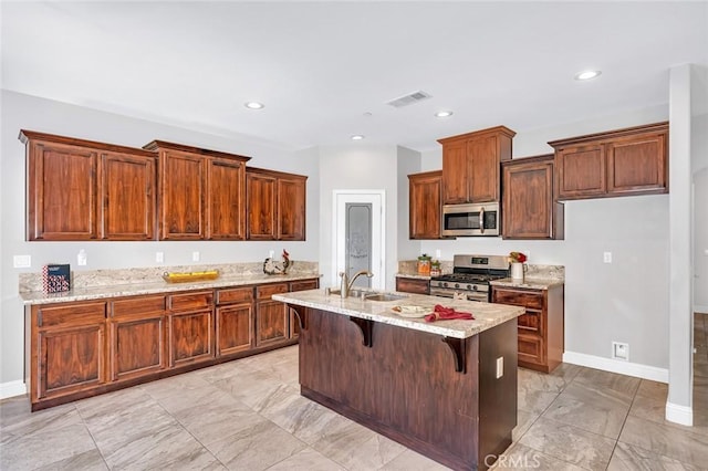 kitchen featuring a breakfast bar area, light stone countertops, an island with sink, a sink, and appliances with stainless steel finishes