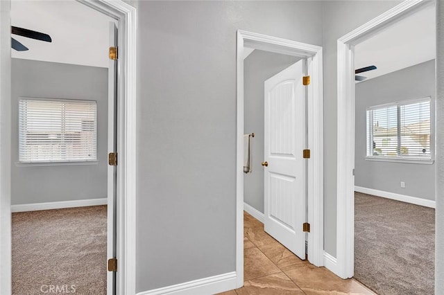 hallway featuring light tile patterned floors, baseboards, and light carpet