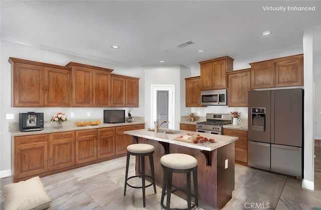 kitchen featuring brown cabinets, an island with sink, a sink, a kitchen breakfast bar, and appliances with stainless steel finishes