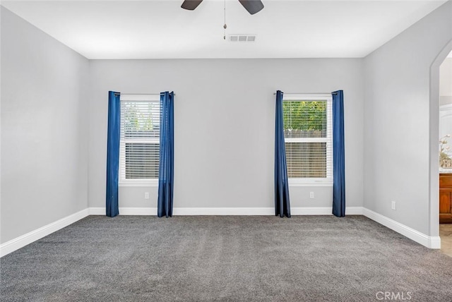 empty room with carpet flooring, arched walkways, visible vents, and baseboards