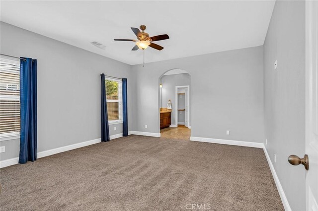 carpeted spare room featuring visible vents, a ceiling fan, arched walkways, and baseboards