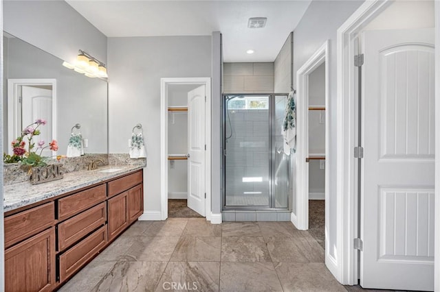 full bathroom featuring a stall shower, vanity, a walk in closet, and baseboards