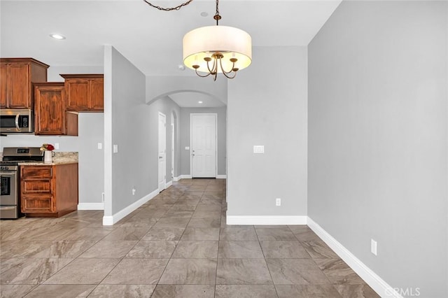 kitchen with recessed lighting, arched walkways, appliances with stainless steel finishes, baseboards, and hanging light fixtures