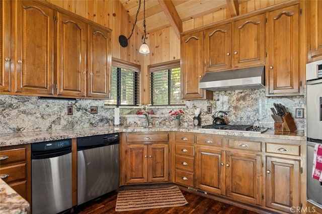 kitchen with vaulted ceiling with beams, under cabinet range hood, brown cabinetry, stainless steel appliances, and a sink