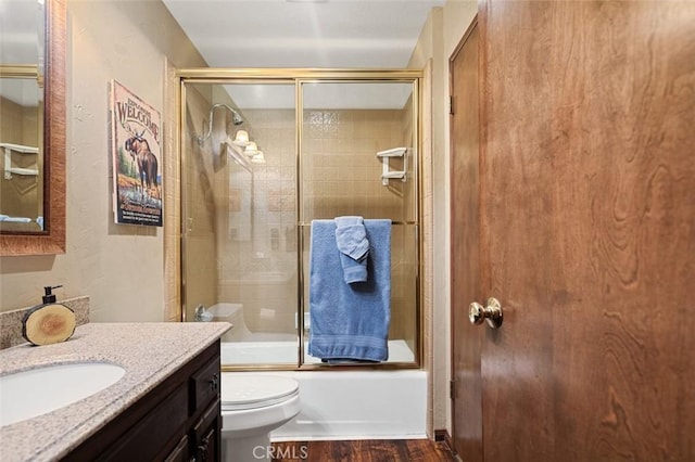 bathroom with wood finished floors, toilet, vanity, and shower / bath combination with glass door