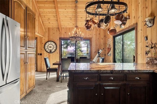 kitchen featuring wood walls, carpet flooring, dark stone countertops, freestanding refrigerator, and an inviting chandelier