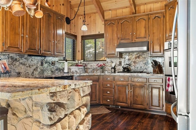 kitchen with under cabinet range hood, light stone counters, lofted ceiling with beams, stainless steel appliances, and dark wood-style flooring