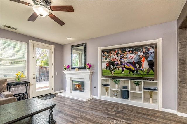 living room featuring a glass covered fireplace, wood finished floors, visible vents, and a wealth of natural light