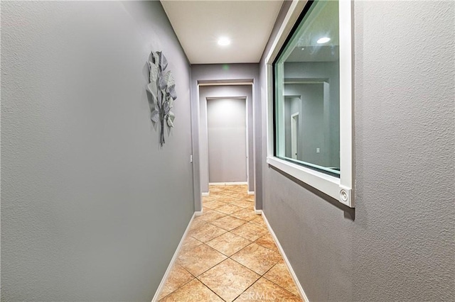 hallway with light tile patterned floors, a textured wall, and baseboards