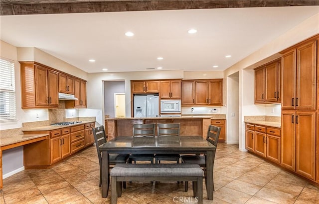 kitchen with light stone countertops, under cabinet range hood, recessed lighting, brown cabinets, and white appliances