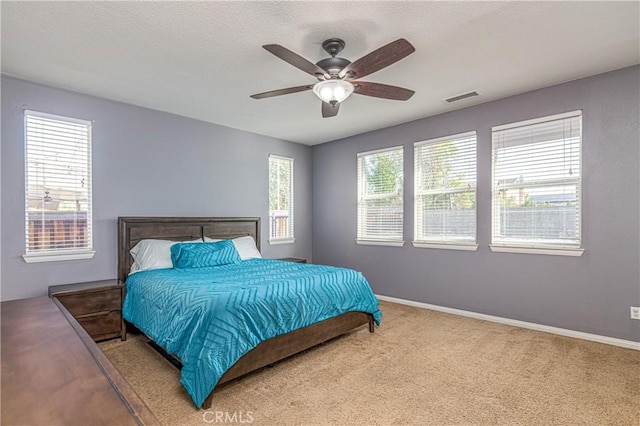 carpeted bedroom with visible vents, multiple windows, baseboards, and ceiling fan