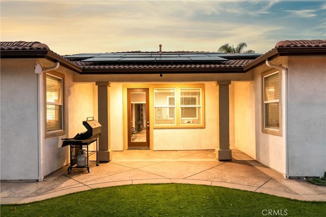 rear view of property with roof mounted solar panels, stucco siding, a tile roof, and a patio