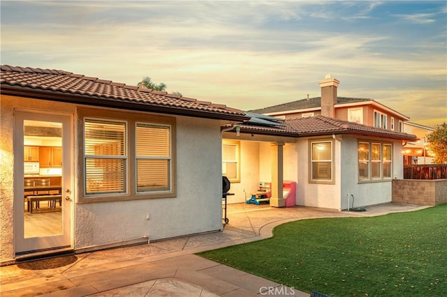 back of property at dusk featuring stucco siding, a patio, a yard, and roof mounted solar panels