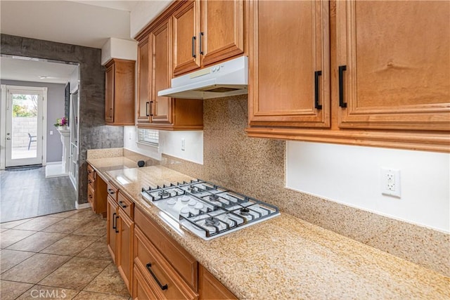 kitchen featuring backsplash, white gas cooktop, under cabinet range hood, light tile patterned floors, and brown cabinets