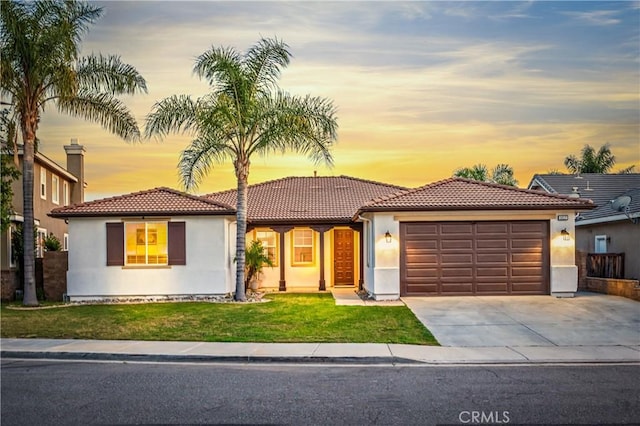 view of front of home featuring driveway, stucco siding, a garage, a tiled roof, and a lawn