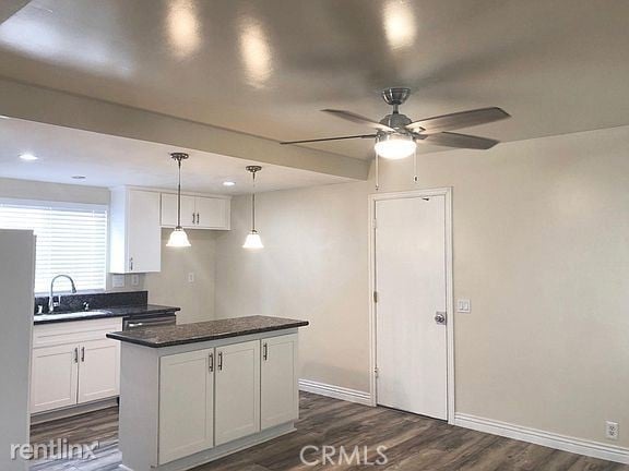 kitchen with dark wood-type flooring, a sink, a center island, white cabinetry, and baseboards