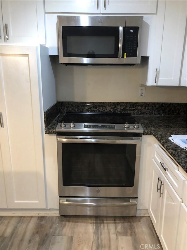 kitchen featuring light wood-type flooring, stainless steel appliances, dark stone countertops, and white cabinetry