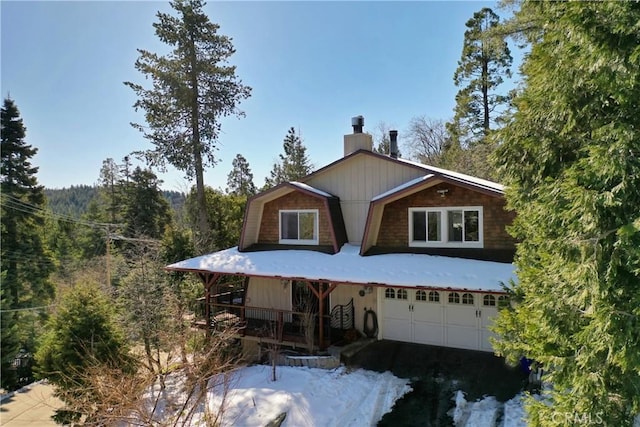 view of front of house with a forest view, driveway, a chimney, and a garage